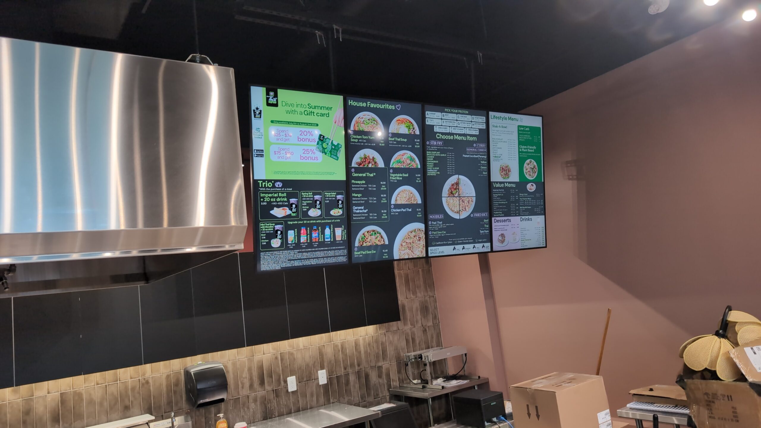 Four digital menu screens beside the kitchen hood at Thai Express in Brockville.